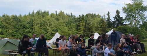 Eine Gruppe Jugendlicher sitzen in Reihen in der Natur und auf Bänken. 898c8c50bc66091df847751e70ec4a567d83bc0f