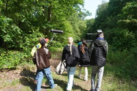 Eine Gruppe Jugendlicher geht mit Kamera und Filmausstatung durch den Wald. 660c8e223ea3727a7dae96267561ff730b3ce42a