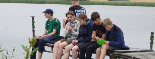 Eine Gruppe Jugendlicher sitzt an einem Steg eines Flusses. 56a765a7a1a35bcf8c66c6fcf81879d587116f39