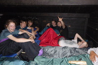 Eine Gruppe Jugendlicher sitzen bei Nacht in einem Shelter mit Schlafsäcken und lassen den Abend ausklingen. 225dacbd0ca1fc7f6316c93e60062d16b1a7a893