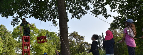 Eine Gruppe Kinder haben einen selbstgemachten Flaschenzug gebaut und versuchen damit möglichst viele Kisten aufeinander zu stapeln. 9fc8ee4c16cab5a637b13e7423e998e9c9efbbba