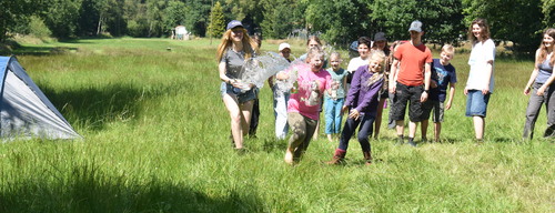 Eine Gruppe Kinder wird von einer Teamerin mit Wasser abgeworfen, während die Sonne scheint. 874cb852f43c9e8dc754f898a95a500bfb8670ce