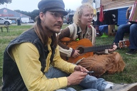 Zwei Teilnehmer*innen sitzen auf dem Theatergelände und spielen Gitarre. F737a0d4e0bc1d2b5c6a60d9a7cc5c273f6706dd